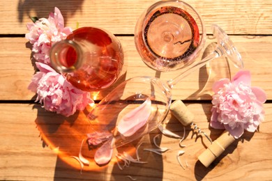 Bottle and glass of rose wine near beautiful peonies on wooden table, flat lay