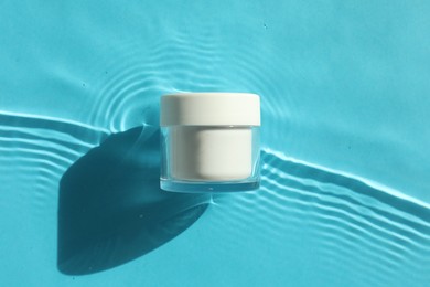 Jar with moisturizing cream in water on light blue background, top view