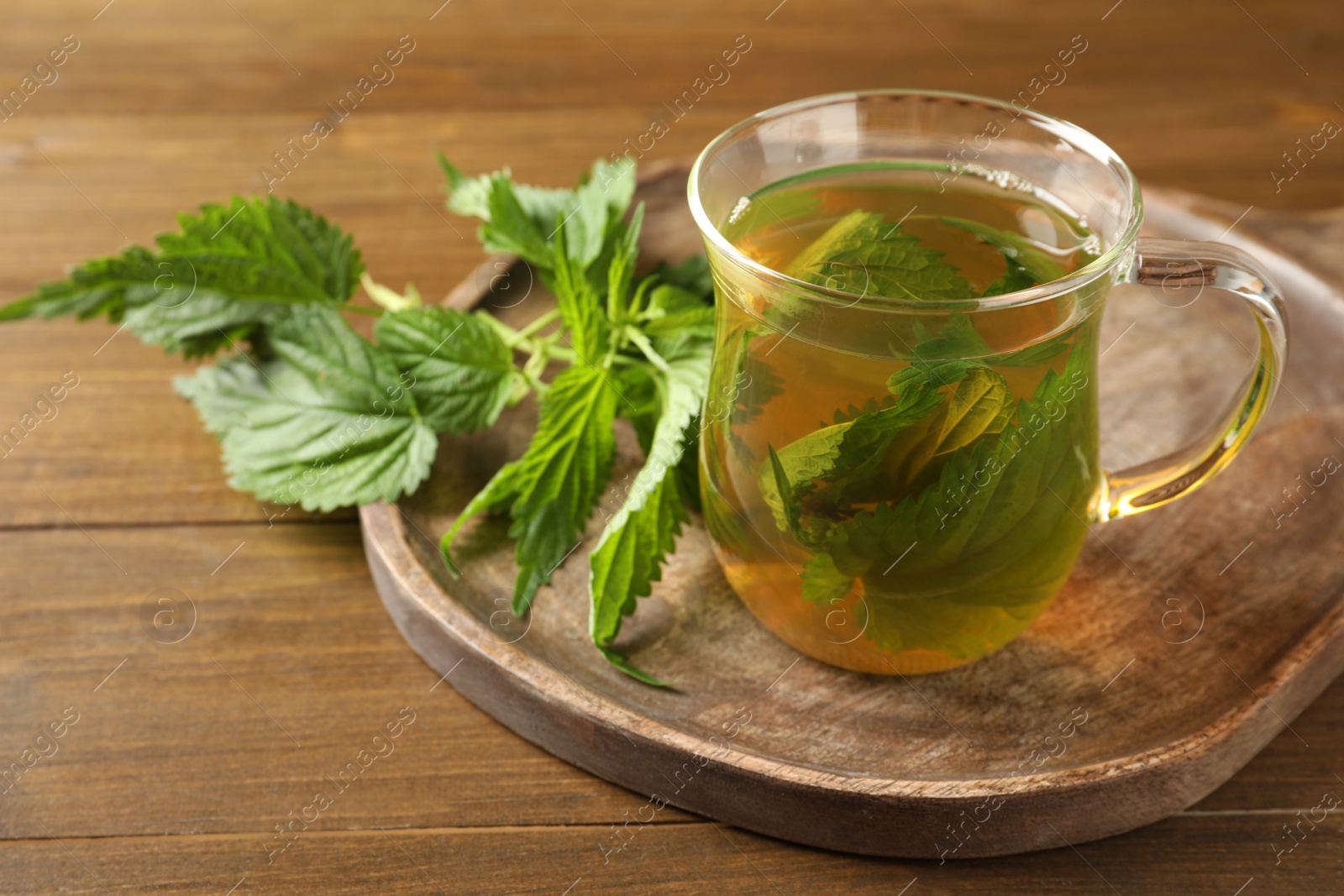 Photo of Glass cup of aromatic nettle tea and green leaves on wooden table