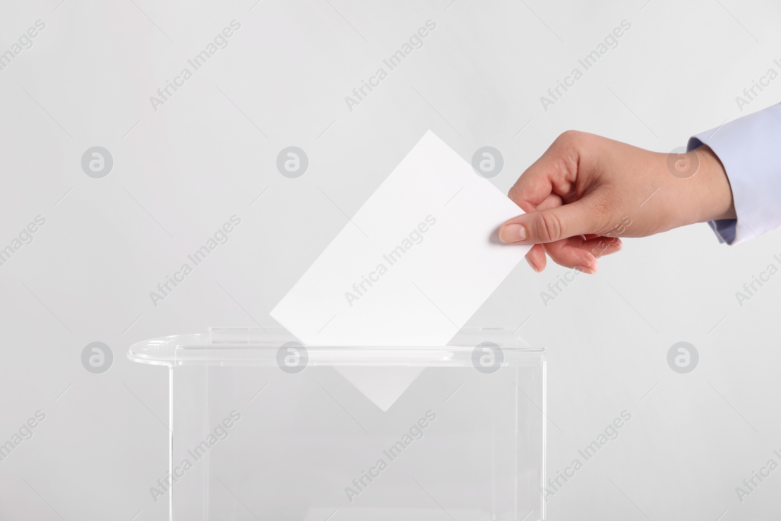 Photo of Woman putting her vote into ballot box on light grey background, closeup