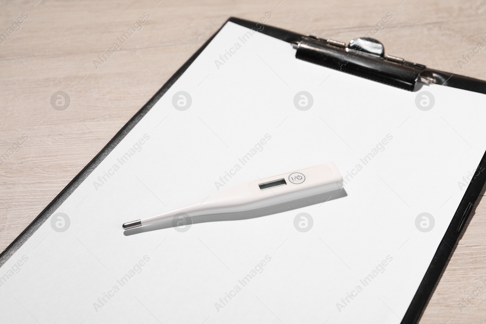 Photo of Clipboard and thermometer on wooden table, closeup. Medical treatment