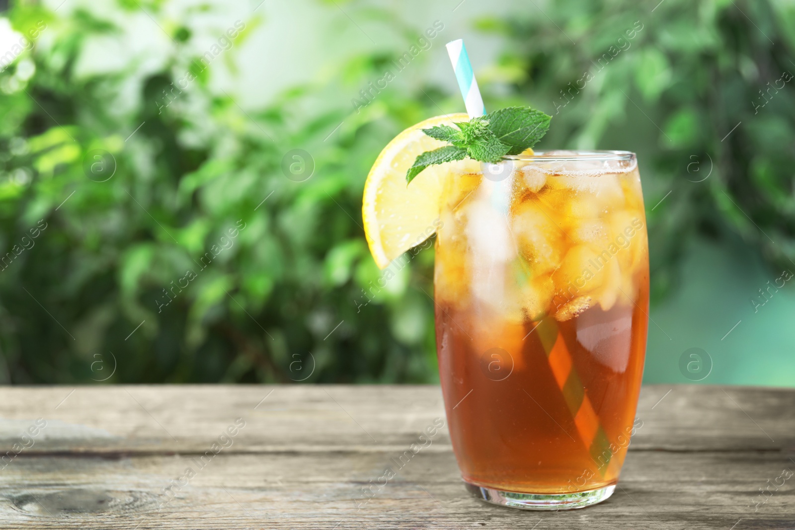 Photo of Delicious iced tea in glass on wooden table outdoors, space for text