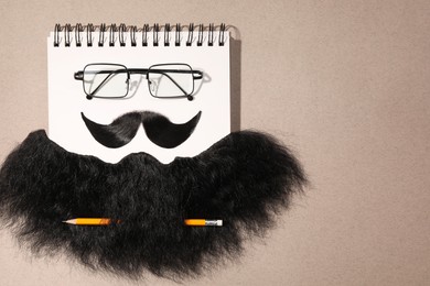 Flat lay composition with artificial moustache and glasses on light brown background, space for text