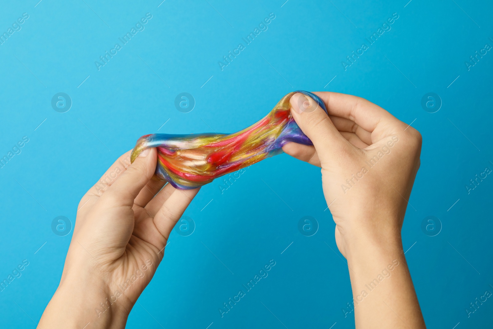 Photo of Woman playing with colorful slime on light blue background, closeup. Antistress toy