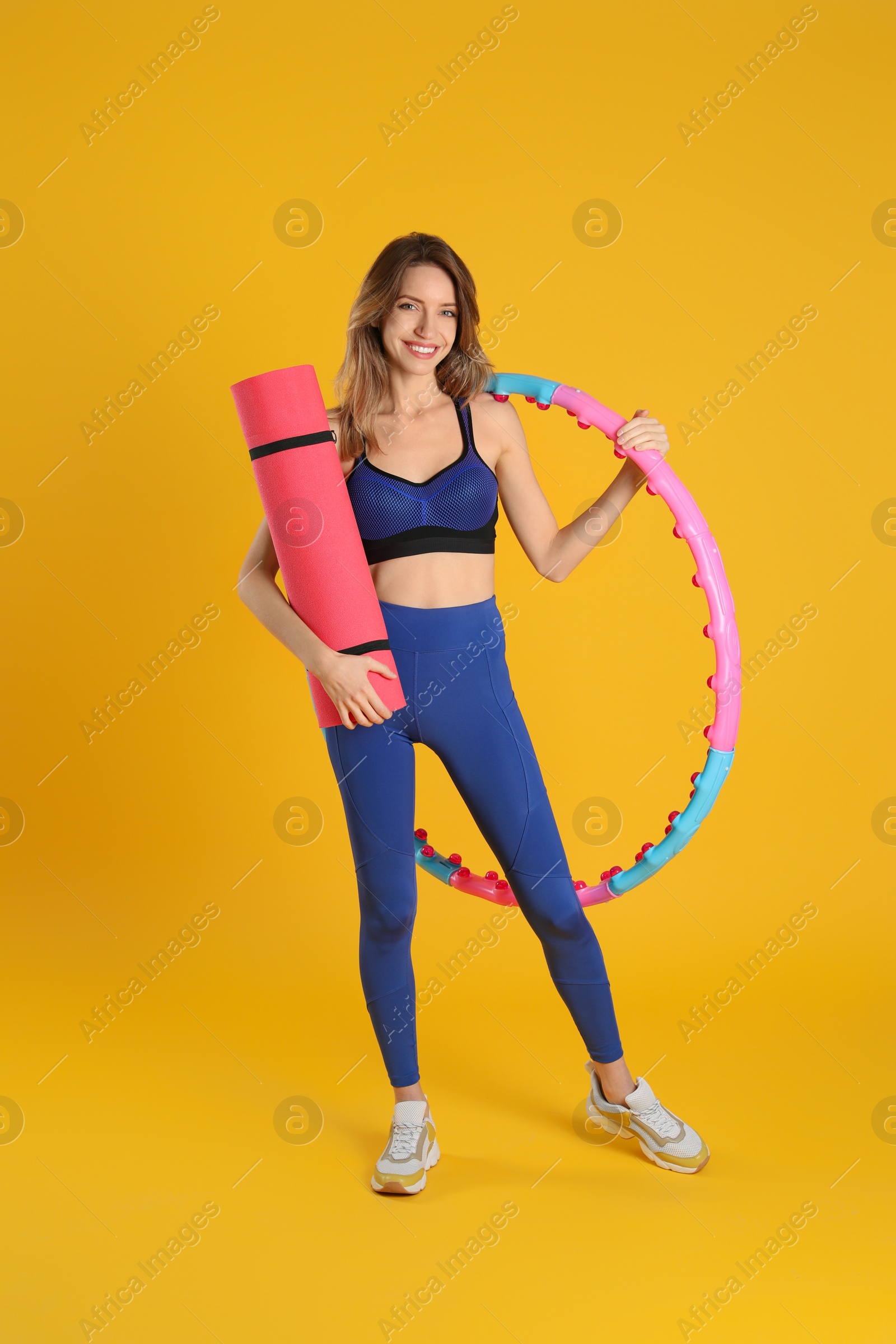 Photo of Beautiful  woman with yoga mat and hula hoop on yellow background