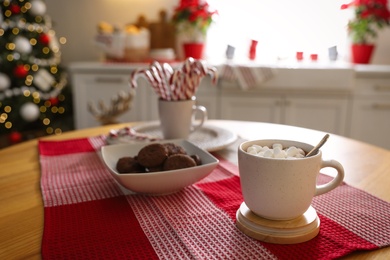 Photo of Delicious marshmallow cocoa on table in kitchen decorated for Christmas