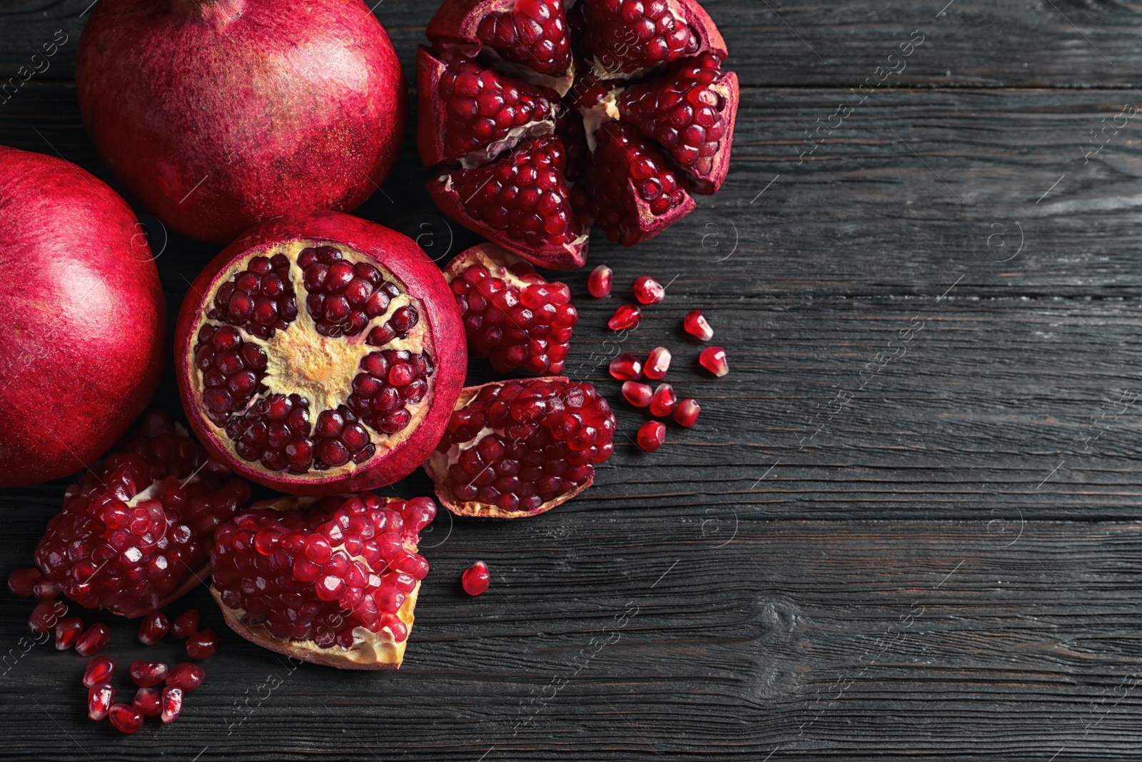 Photo of Ripe pomegranates and seeds on wooden background, flat lay with space for text