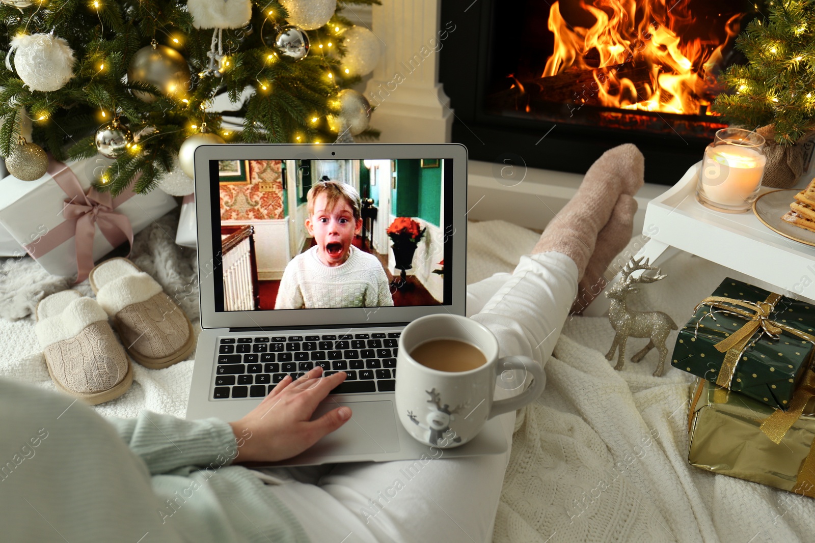 Photo of MYKOLAIV, UKRAINE - DECEMBER 23, 2020: Woman with sweet drink watching Home Alone movie on laptop at home, closeup. Cozy winter holidays atmosphere