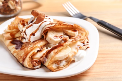 Thin pancakes served with chocolate syrup, cream and banana on plate