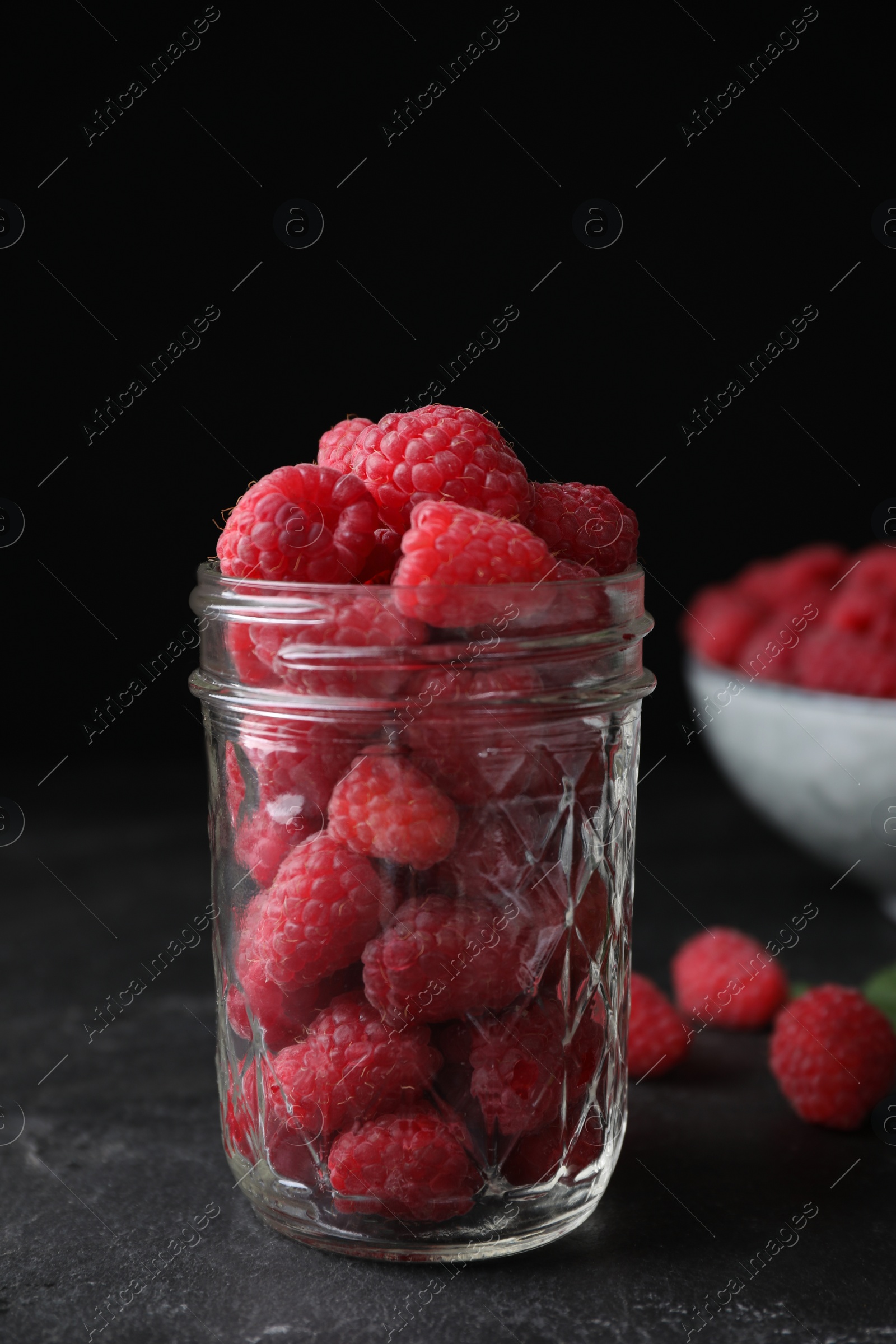 Photo of Delicious fresh ripe raspberries in glass jar on black table