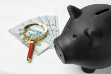 Photo of Black piggy bank, money and magnifying glass on table