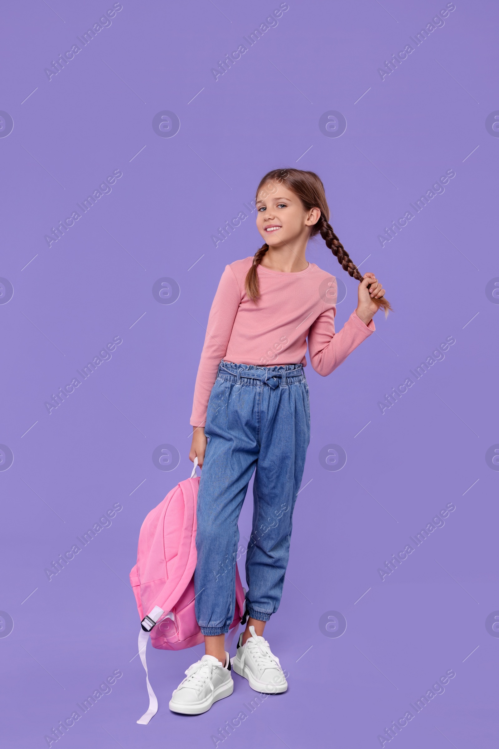 Photo of Happy schoolgirl with backpack on violet background