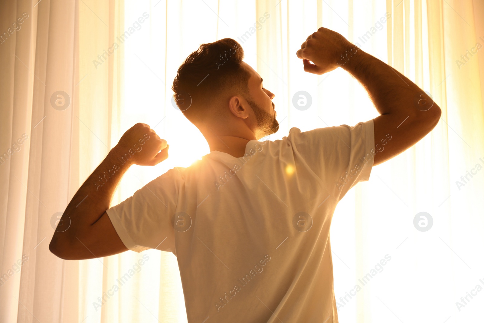 Photo of Young man stretching near window at home. Lazy morning