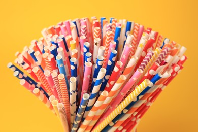 Many paper drinking straws on orange background, closeup