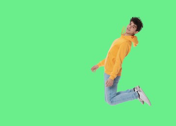 Teenage boy jumping on green background, space for text