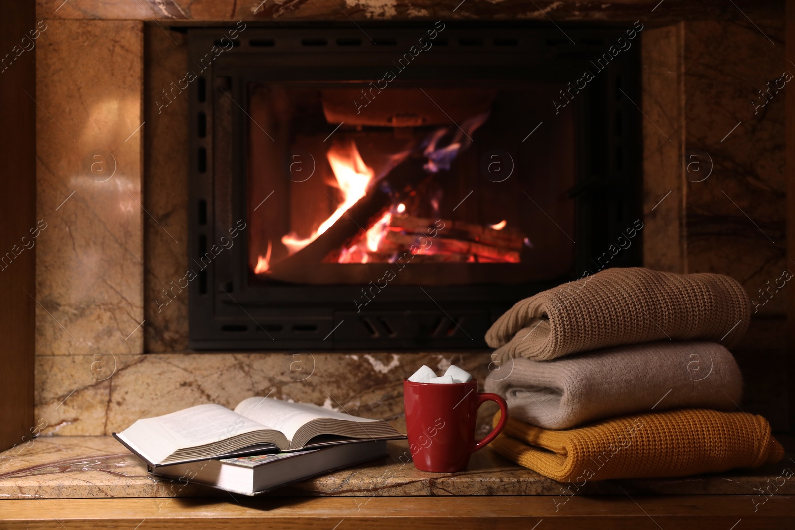 Photo of Stack of warm sweaters, cup, books and fireplace indoors