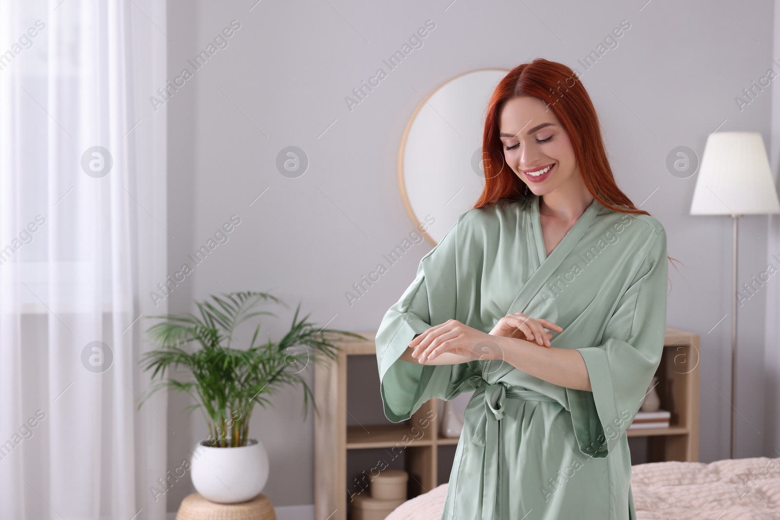 Photo of Beautiful young woman touching her smooth arms in bedroom, space for text