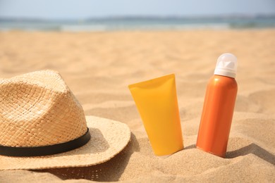Photo of Sunscreens and straw hat on sandy beach, space for text. Sun protection