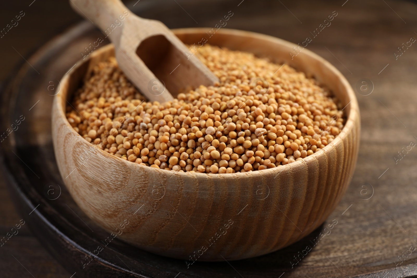 Photo of Mustard seeds with wooden bowl and scoop on tray, closeup