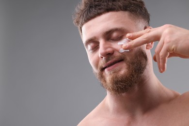 Photo of Handsome man applying moisturizing cream onto his face on grey background, space for text