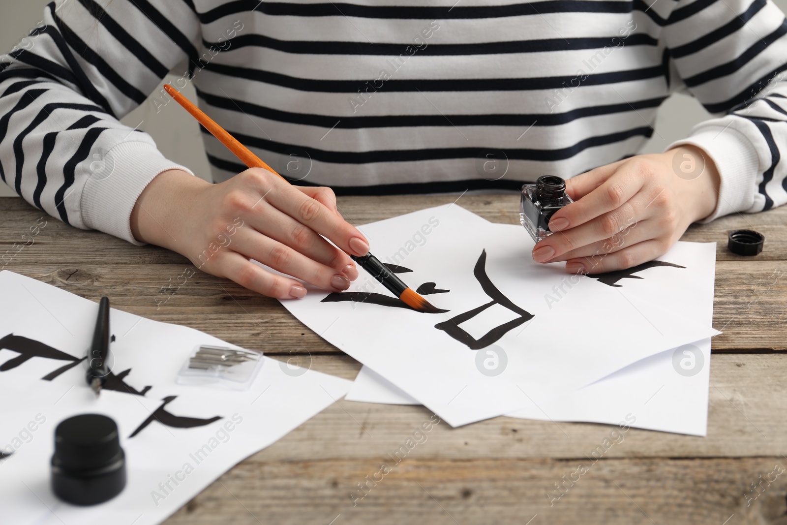 Photo of Calligraphy. Woman with brush and inkwell writing hieroglyphs on paper at wooden table, closeup
