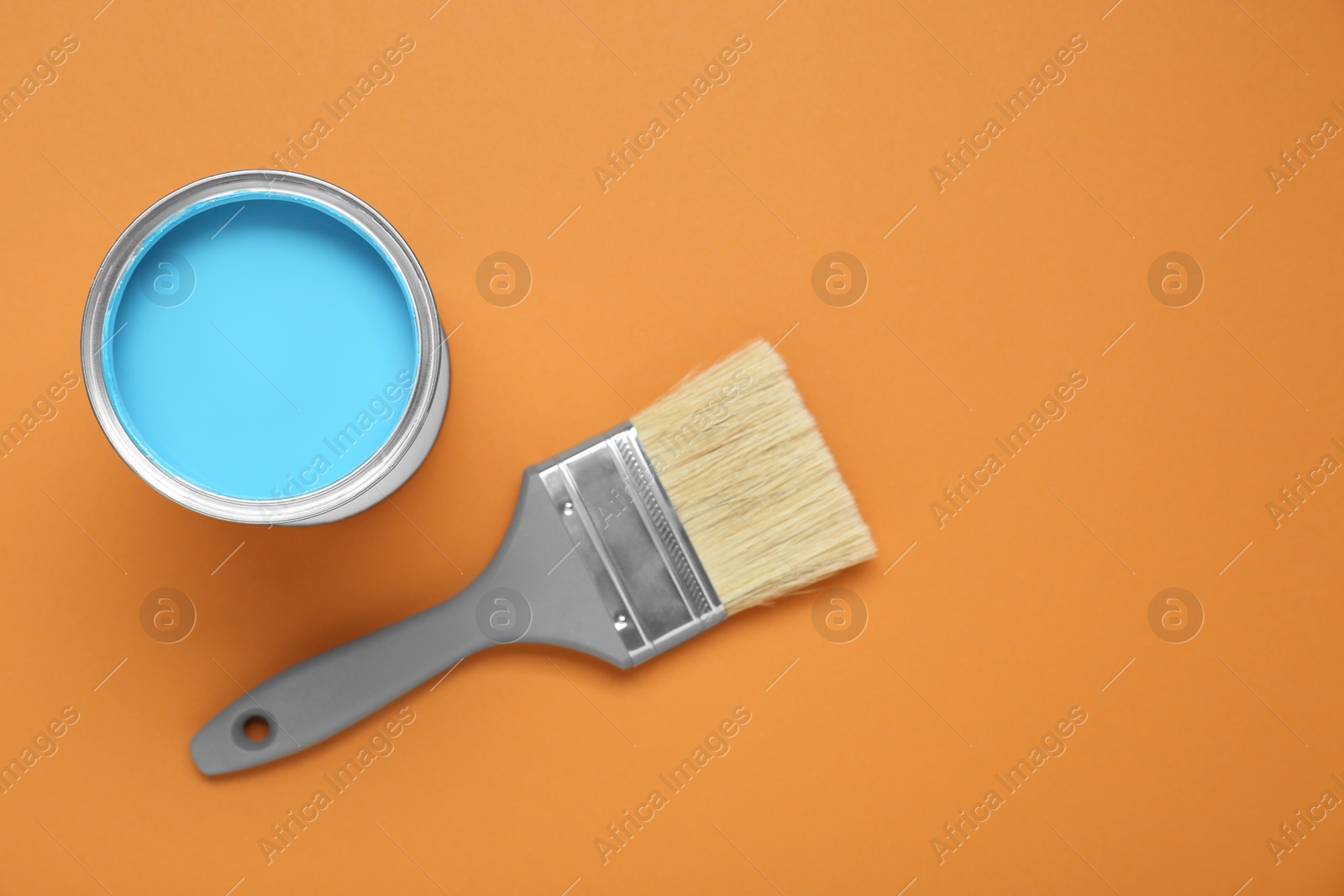 Photo of Can of light blue paint and brush on pale orange background, flat lay. Space for text