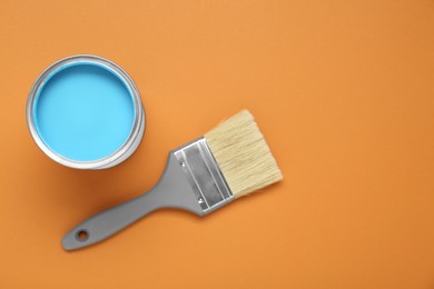 Photo of Can of light blue paint and brush on pale orange background, flat lay. Space for text