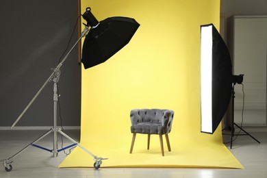 Photo of Yellow photo background, armchair and professional lighting equipment in modern studio