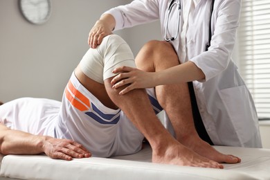 Photo of Sports injury. Doctor examining patient's knee in hospital, closeup