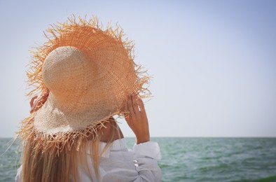 Photo of Young woman with straw hat near sea on sunny day in summer, space for text