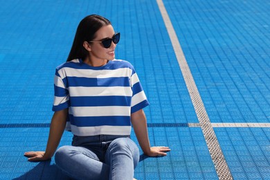 Photo of Beautiful smiling woman in sunglasses on blue floor covering outdoors, space for text