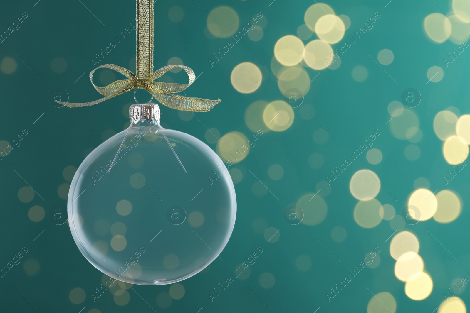 Photo of Transparent glass Christmas ball with golden ribbon and bow against green background. Space for text