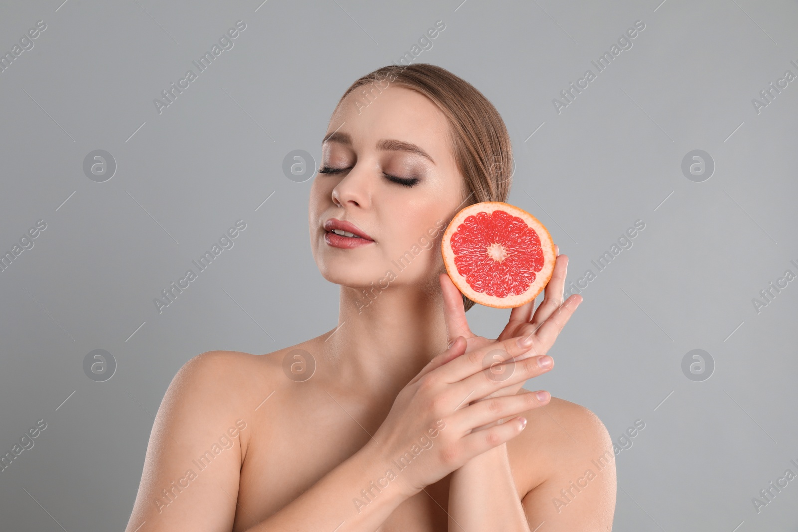 Photo of Young woman with cut grapefruit on grey background. Vitamin rich food