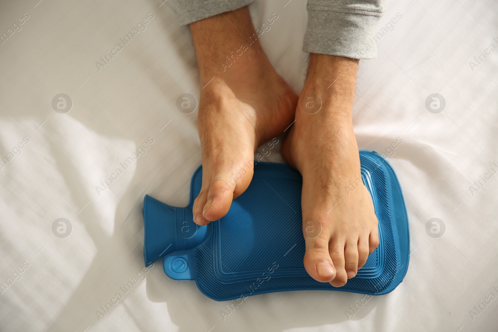 Photo of Man warming feet with hot water bottle on bed, closeup