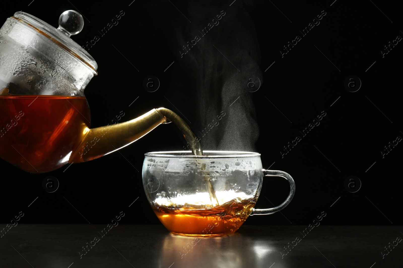 Photo of Pouring delicious hot tea into glass cup on table against dark background