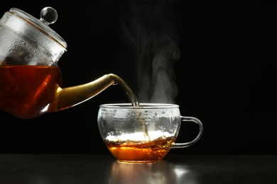 Photo of Pouring delicious hot tea into glass cup on table against dark background