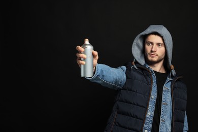 Handsome man holding used can of spray paint on black background. Space for text