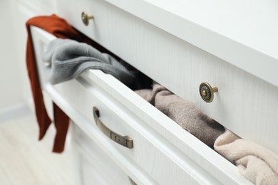 Cluttered chest of drawers indoors, closeup. Clothes in mess