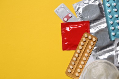 Photo of Contraceptive pills and condoms on yellow background, flat lay with space for text. Different birth control methods