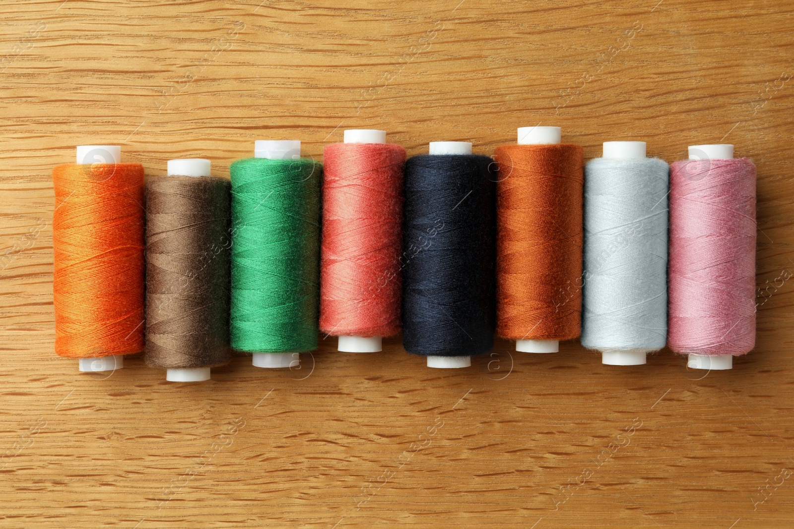 Photo of Many colorful sewing threads on wooden table, flat lay