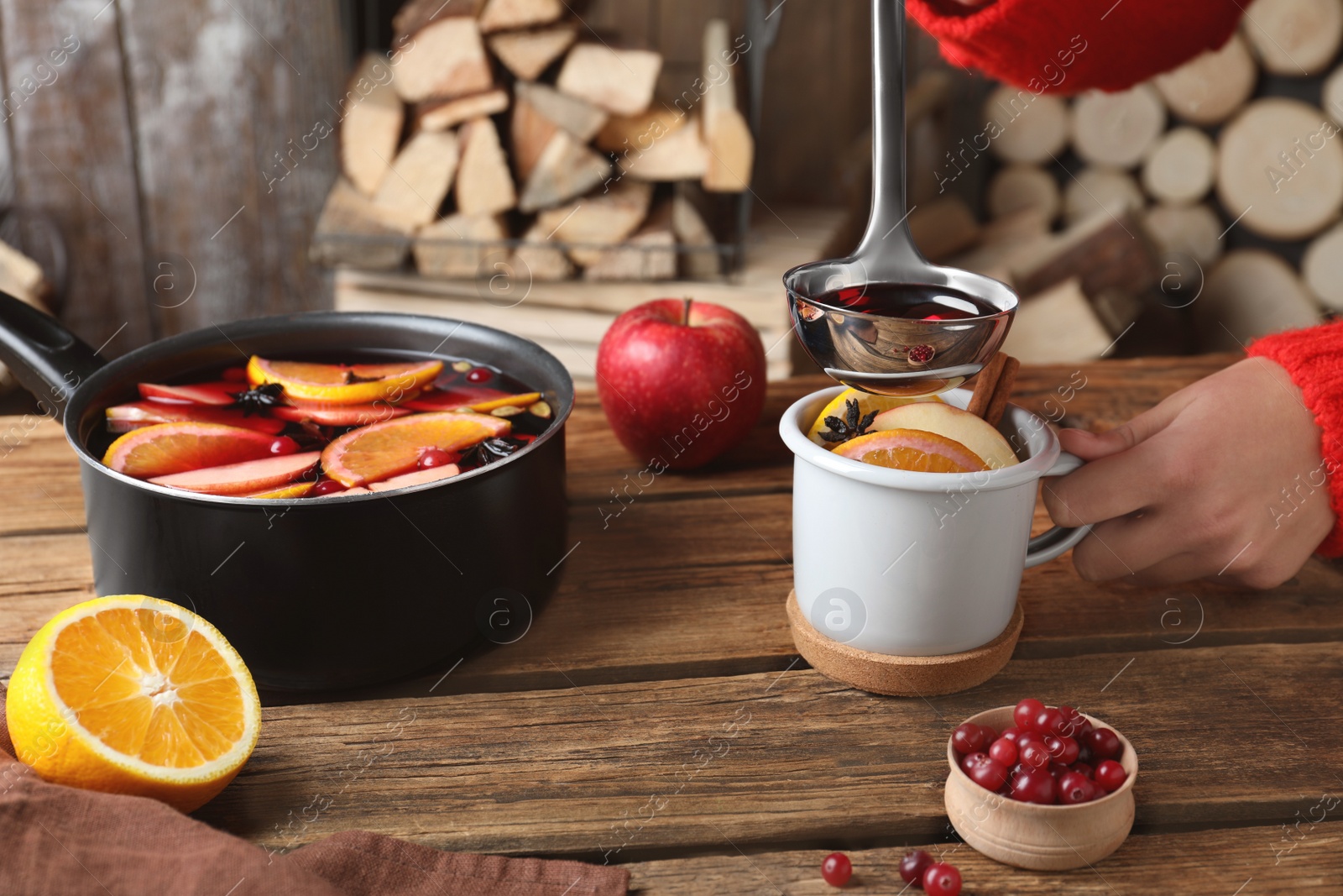 Photo of Woman pouring hot mulled wine into cup at wooden table, closeup