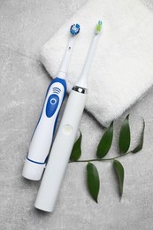 Photo of Electric toothbrushes, towel and leaves on grey textured table, flat lay