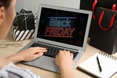 Photo of Woman using laptop with Black Friday announcement at wooden table, closeup