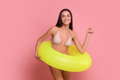 Young woman in stylish bikini with inflatable ring on pink background