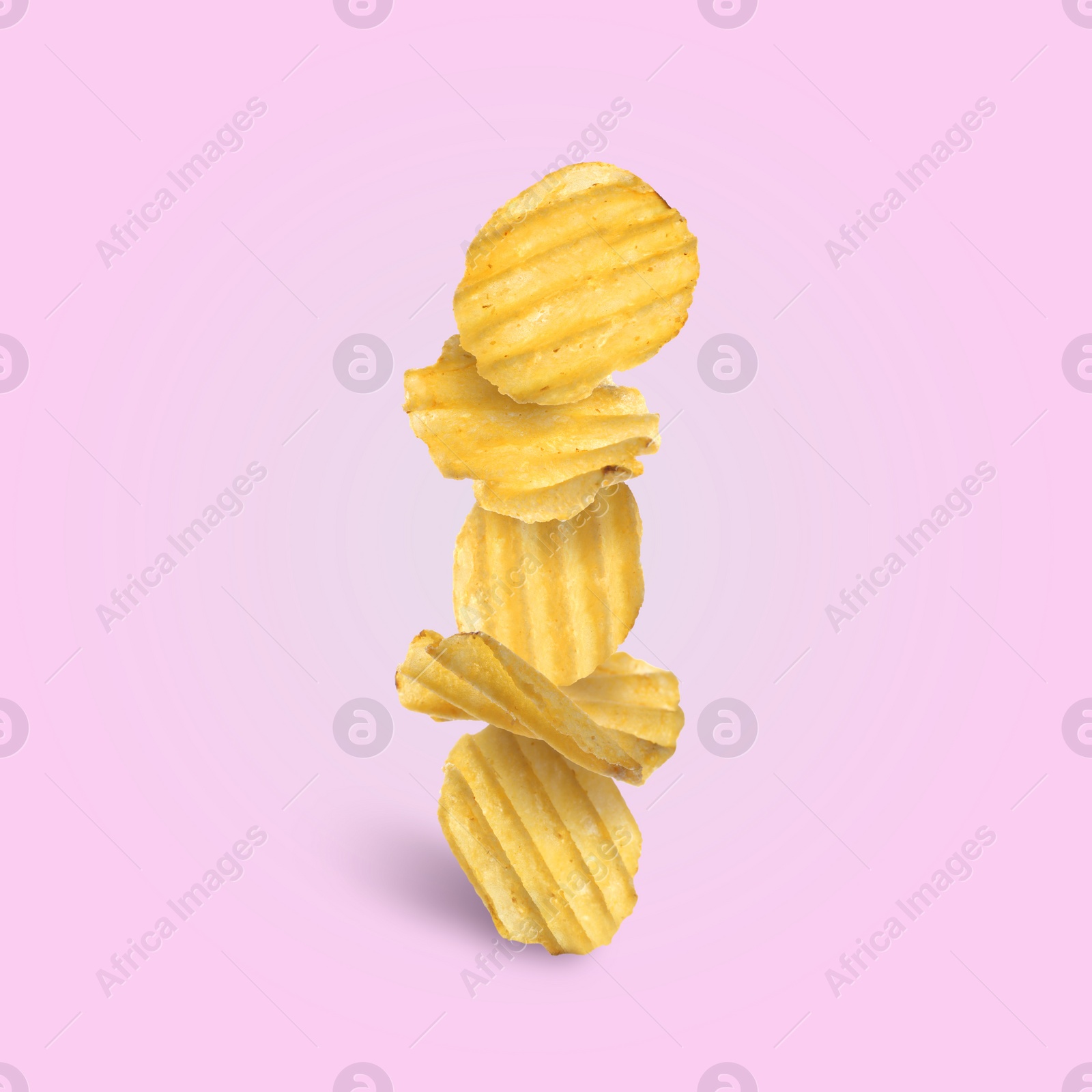 Image of Tasty ridged potato chips falling on pale light violet background