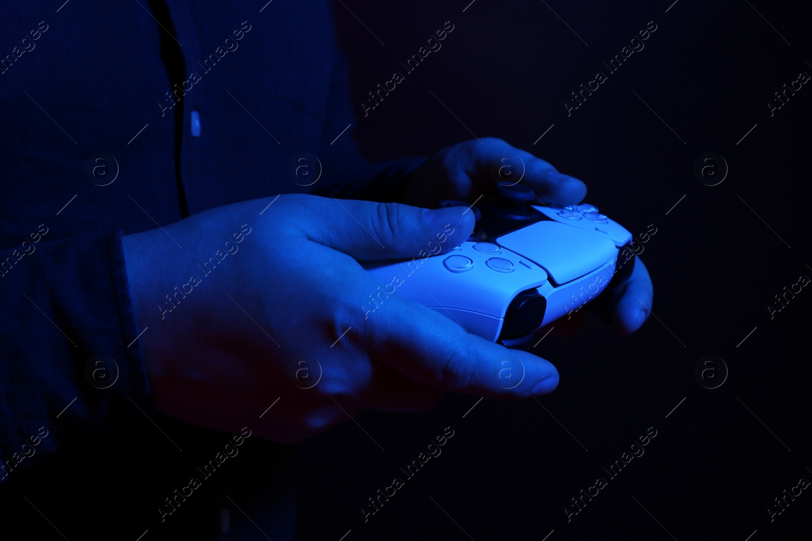 Photo of Man using wireless game controller on dark background in neon lights, closeup