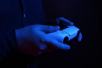 Photo of Man using wireless game controller on dark background in neon lights, closeup