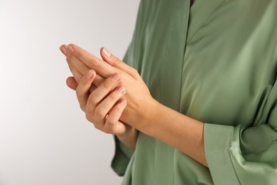 Photo of Woman applying cosmetic cream onto hand on light grey background, closeup