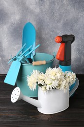 Photo of Watering can, gardening tools and beautiful flowers on wooden table against light grey background