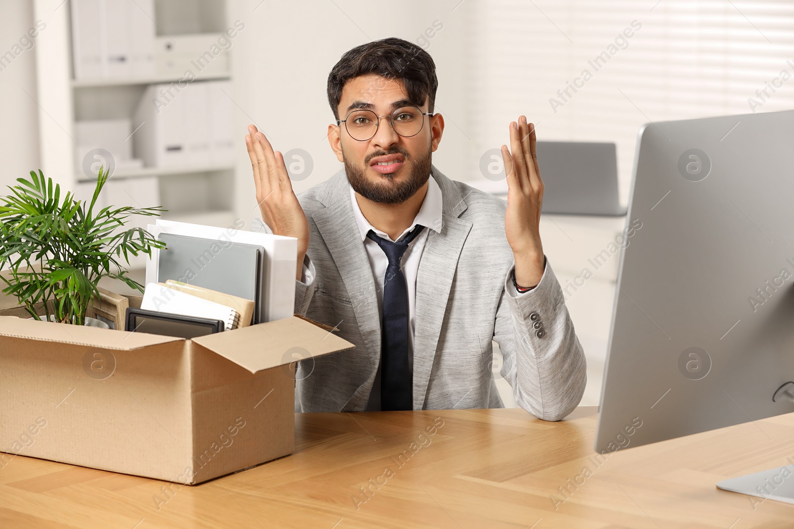 Photo of Unemployment problem. Frustrated man with box of personal belongings at desk in office